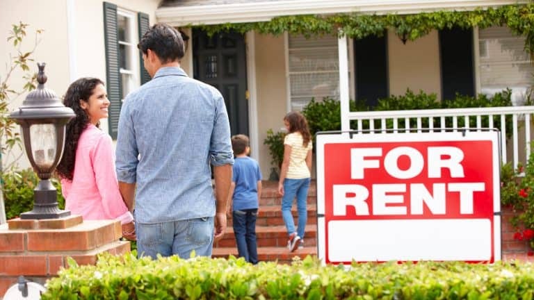 A family standing in front of a house with a for rent sign.