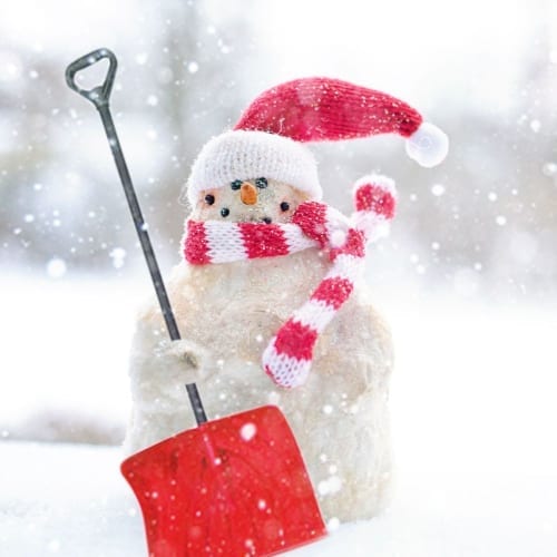 A snowman holding a red shovel in the snow.