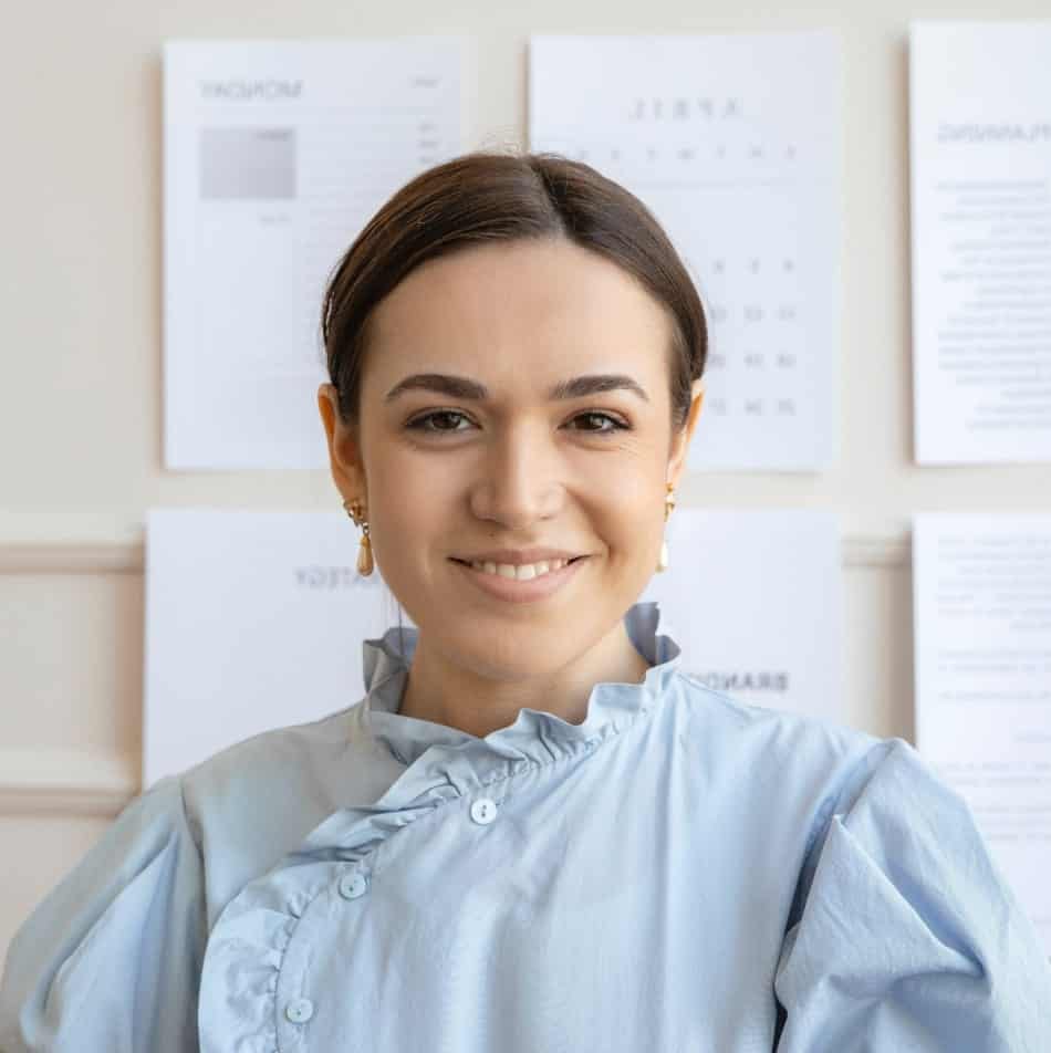 A smiling woman in a blue shirt standing in front of some papers.