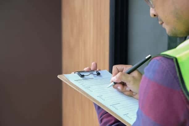 A man in a vest writing on a clipboard.
