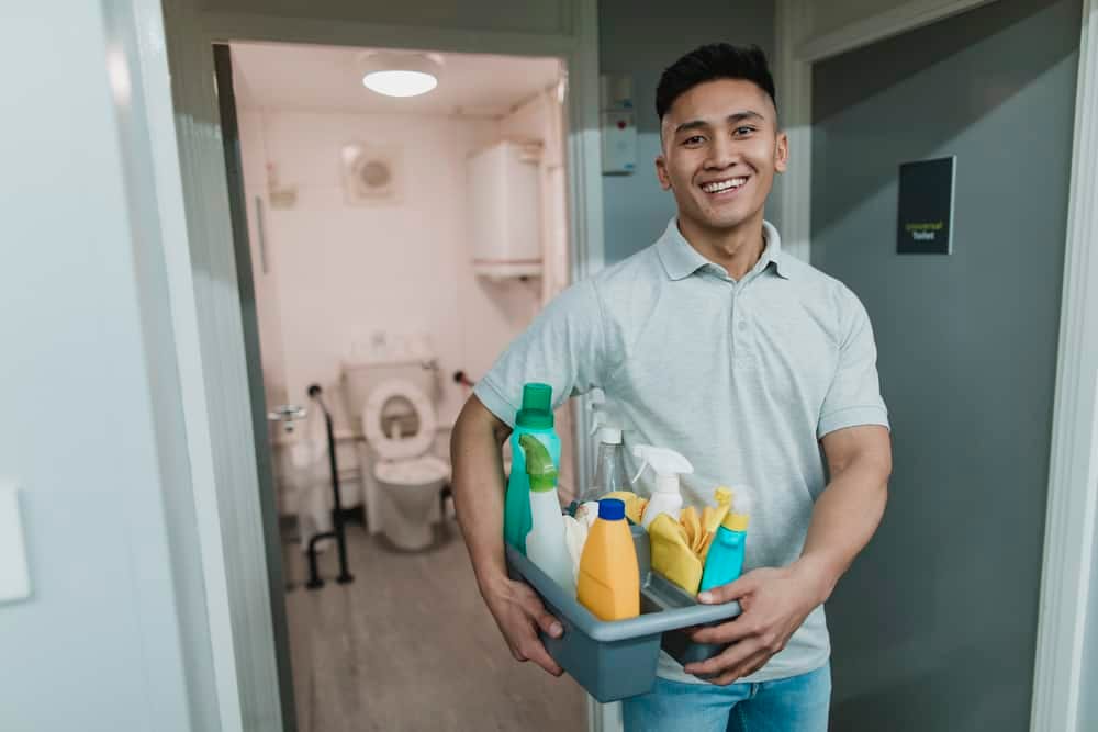 A man holding a basket of cleaning supplies in a hallway.