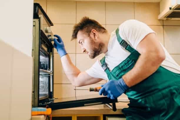 A man fixing an oven in a kitchen.