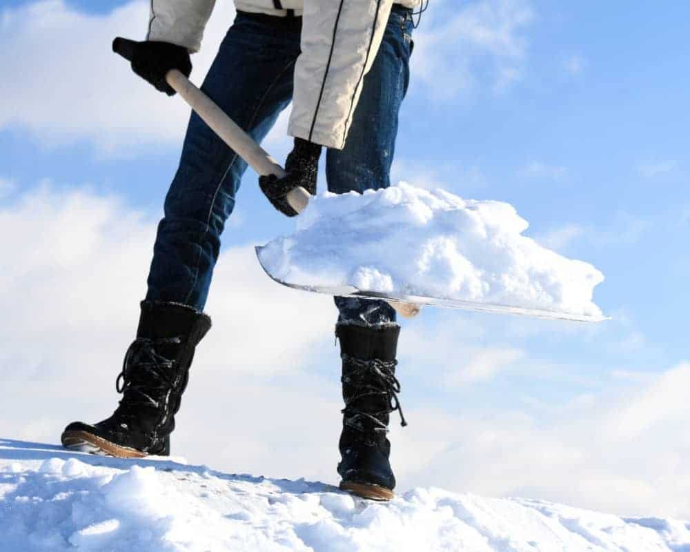 A person holding a snow shovel on top of a snowy hill.