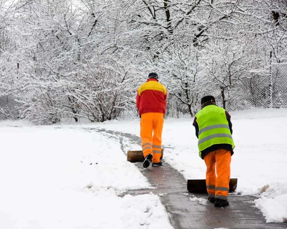 Two men shoveling snow in a park.