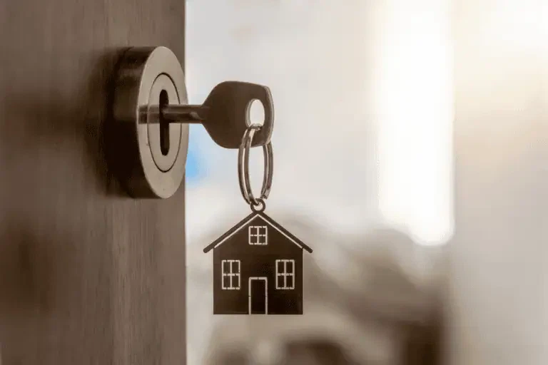 A key inserted into a door lock with a keychain shaped like a house hanging from it.