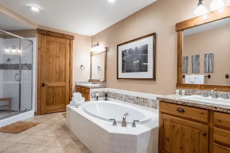 Spacious bathroom with a central bathtub, double sinks, wood cabinets, a glass shower, beige tile flooring, and framed artwork on the walls.