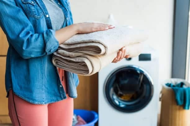 A woman holding towels in front of a washing machine.