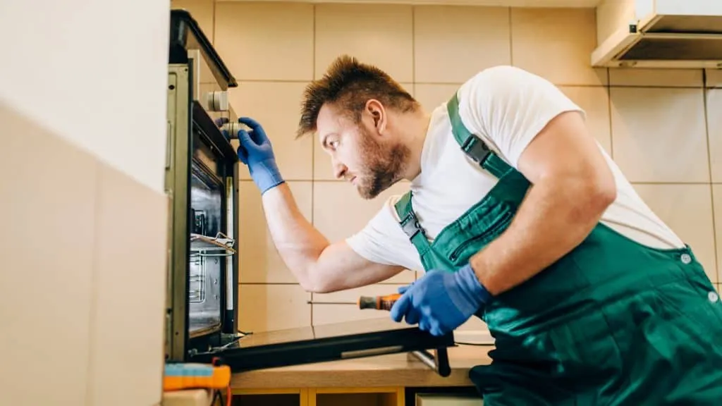 A man fixing an oven in a kitchen.