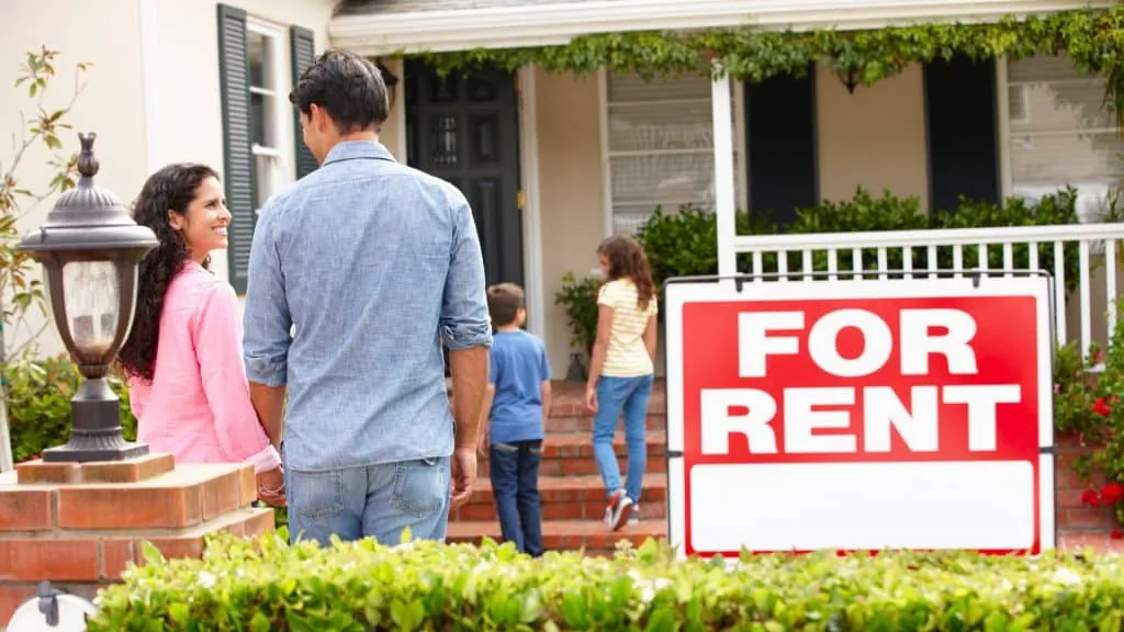 A family standing in front of a house with a for rent sign.