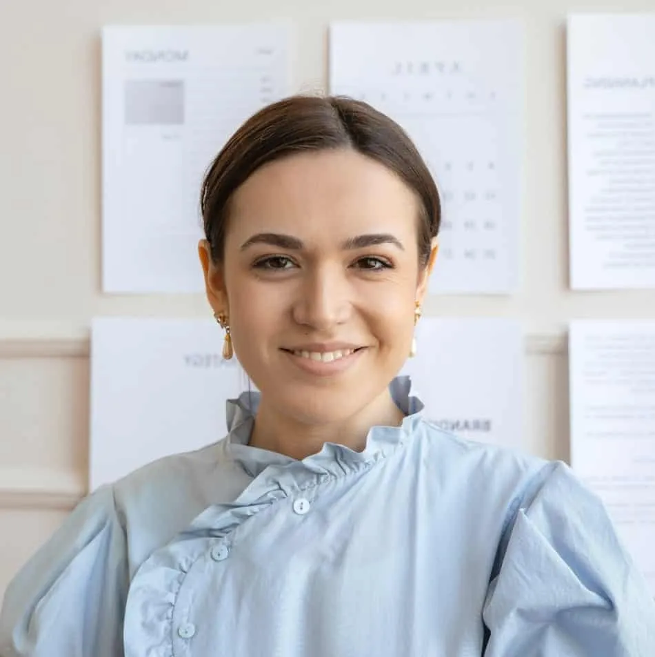A smiling woman in a blue shirt standing in front of some papers.