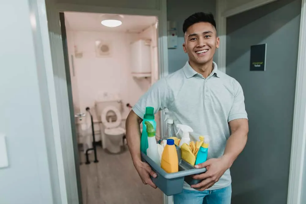 A man holding a basket of cleaning supplies in a hallway.