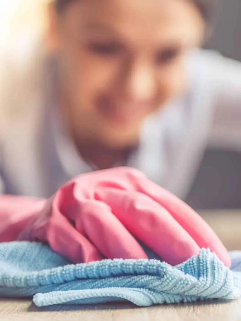 A woman in pink gloves cleaning a cloth on a table in a property management setting.