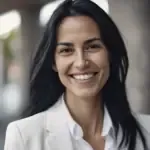 Woman with long dark hair smiling and wearing a white blazer in an outdoor setting.